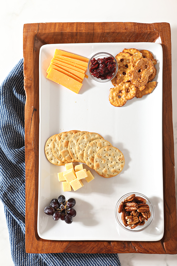 Crackers, cheeses, grapes, nuts and dried cranberries on a white plate before a cheese board is completed