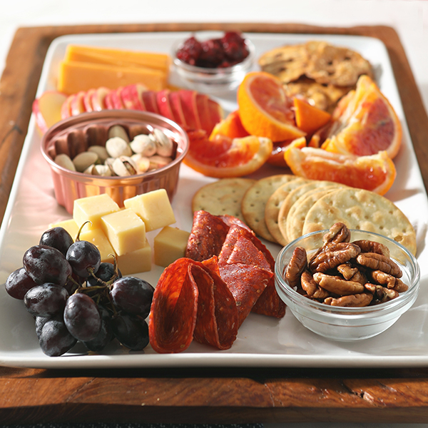 Close up of pepperoni and grapes on a charcuterie board with lots of oranges and reds on a white plate