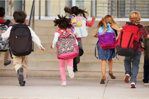 A group of seven children running up stairs, presumably into a school.