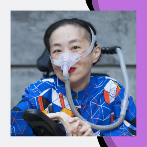 Photo of an Asian American woman in a power chair. She is wearing a blue shirt with a geometric pattern with orange, black, white, and yellow lines and cubes. She is wearing a mask over her nose attached to a gray tube and bright red lip color. She is smiling at the camera. Photo credit: Eddie Hernandez Photography Photo is in front of a light gray background with a purple oblong shape along the right side and a black outline around the shape.