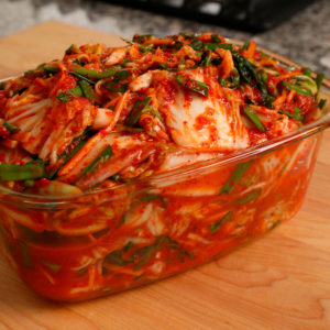 in a glass bowl, on a wooden board, is kimchi, a fermented cabbage dish popular in Korea topped with scallions