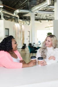 two women chatting over coffee in an office space, likely discussing the latest episode of a reality tv show 