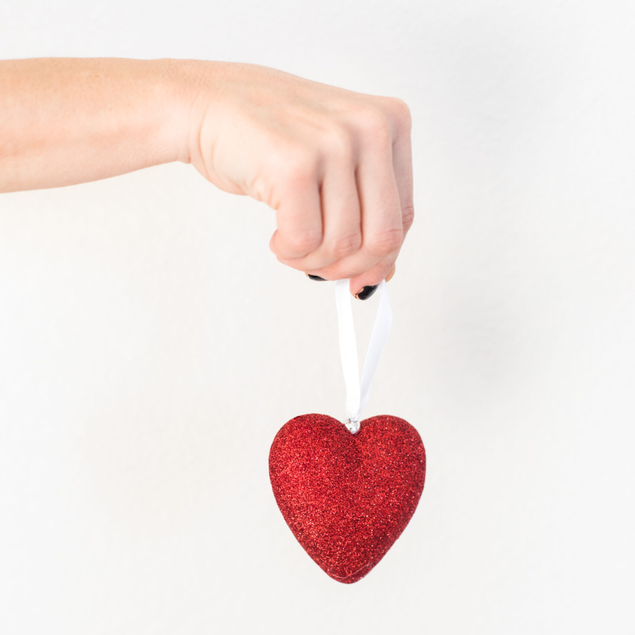 romance tropes - hand holding a red glitter heart ornament