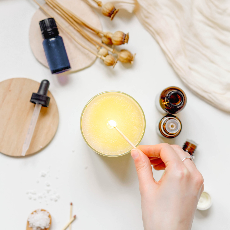 A hand lighting a candle surrounded by essential oils and salt