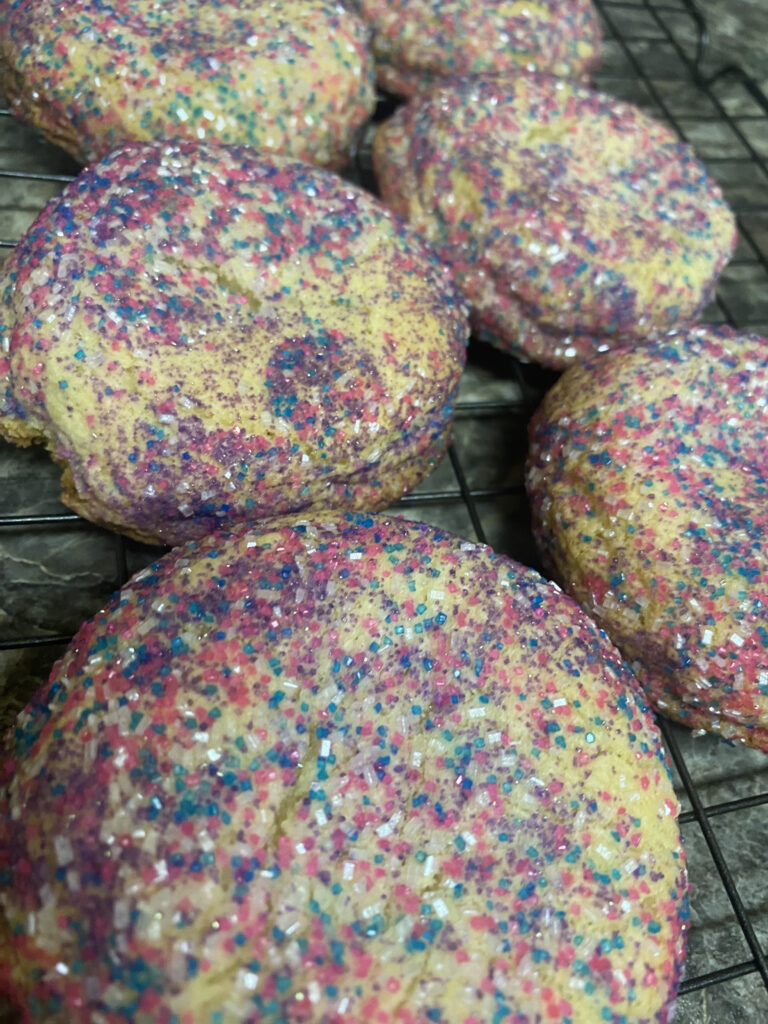 close up shot of six sugar cookies with rainbow sanded sugar on a wire rack