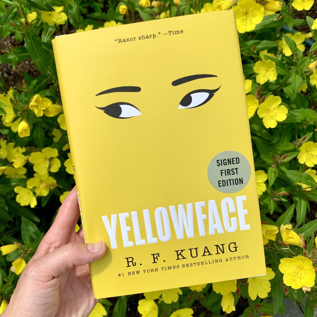 The book Yelloface by R. F. Kuang held over a background of yellow flowers.