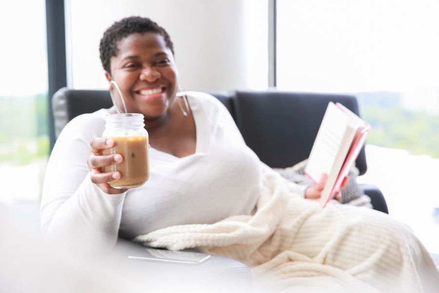 Black femme-presenting person enjoying a book and holding an iced coffee