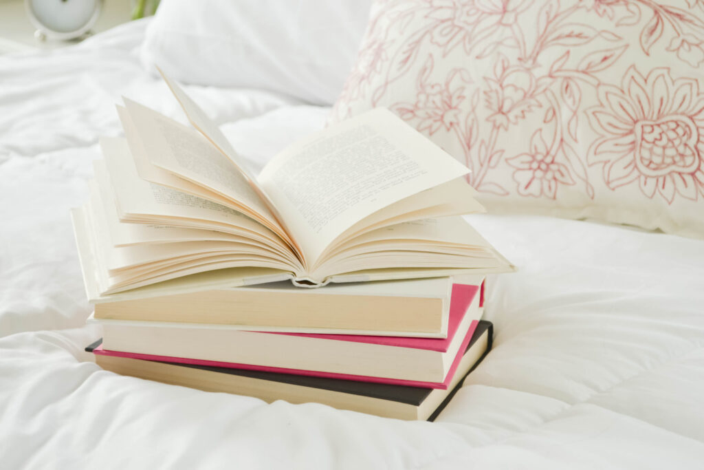 stack of books on a bed, with a pretty floral pillow in the background